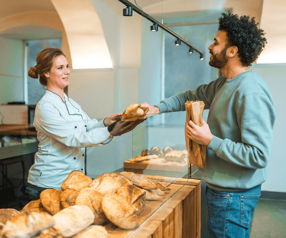 Baker handing bread to customer in bakery.